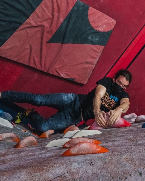 A from-above shot of a climber reaching for colourful holds inside a climbing gym.